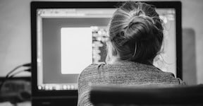 A young woman with a bun hairstyle is working from her computer.