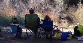 Jason and two youngsters sit in camping chairs with their backs to the camera, looking out at nature.