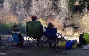 Jason and two youngsters sit in camping chairs with their backs to the camera, looking out at nature.