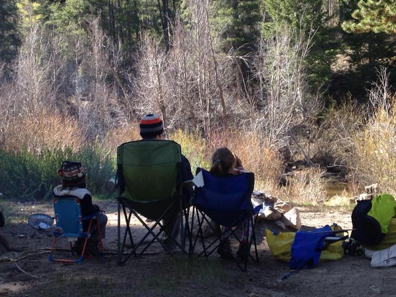 Jason and two youngsters sit in camping chairs with their backs to the camera, looking out at nature.