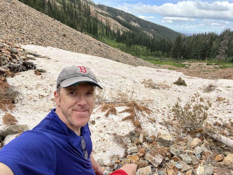 Jason taking a selfie in front of snow still on the mountains in August