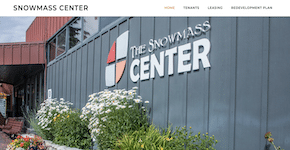Hero image for The Snowmass Center website, featuring the center's logo on the side of a gray building. The outer wall is lined with blooming daisies.
